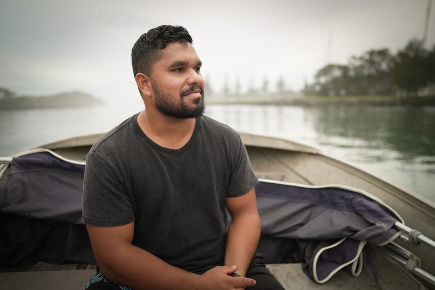 Leeroy sitting in a boat on the water on a cloudy day, looking into the distance.