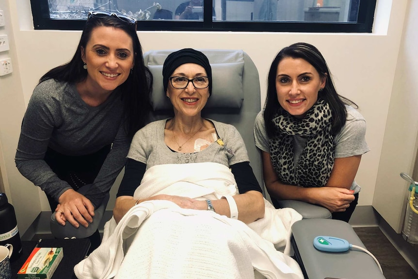 A woman in a hospital bed with her adult daughters on either side.