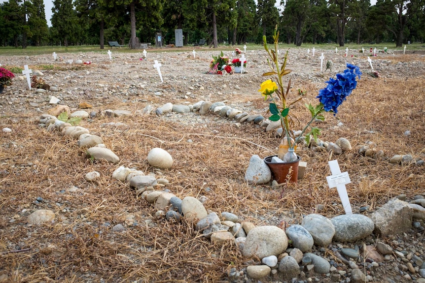 A sandy field with small white crosses and fake plastic flowers sporadically stuck in the ground