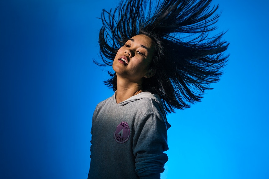 Mid-shot colour photograph of actor and slam poet May Tran posing in front of a blue background.