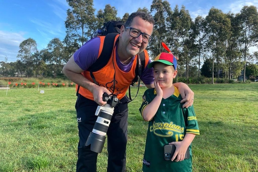 A man with a big camera next to a boy.
