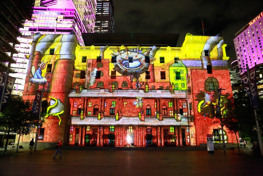 A large building at night is lit up by a colourful work of art projection.
