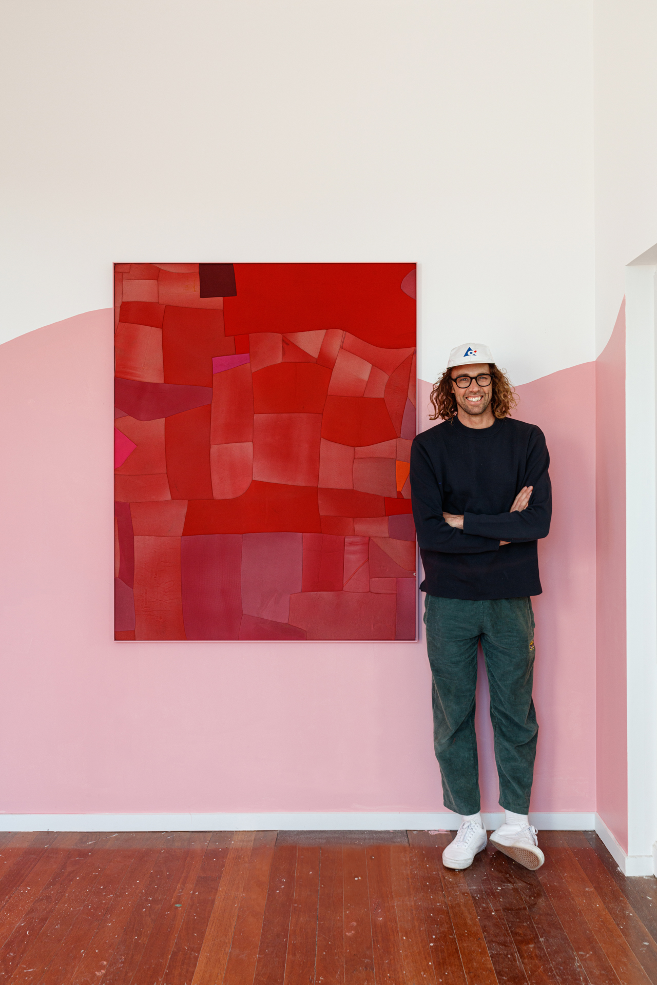 Artist stands next to his pink patchwork painting on the wall in a gallery space 
