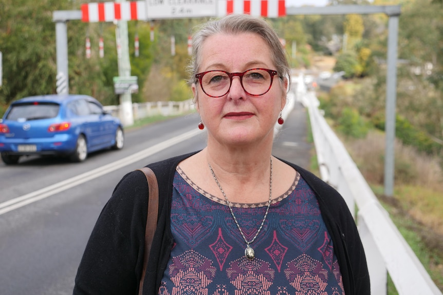 woman in purple shirt stands in front of single-lane white bridge