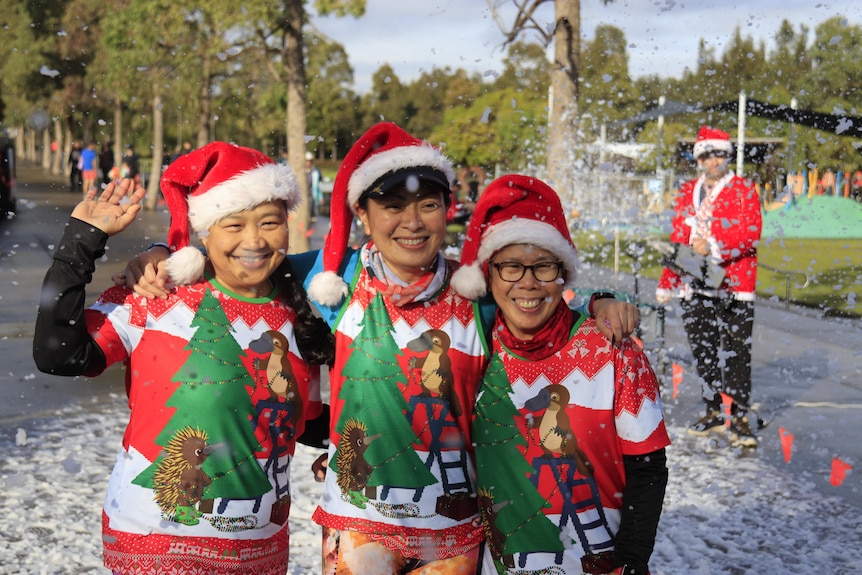 A group of three people in Santa hats with fake snow around them.