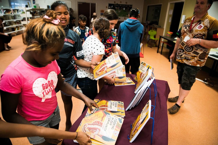 Aboriginal children and teenagers keenly take a look at their local cookbook.