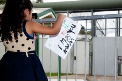 A child stands outside a prison holding a sign that says "I miss you mum".