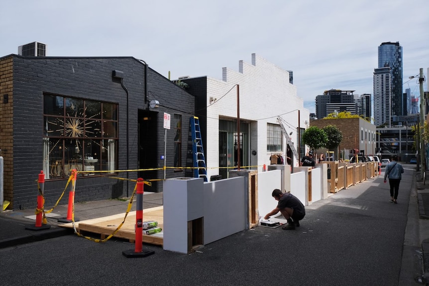 A carpenter prepares an outdoor eating area outside a restaurant.