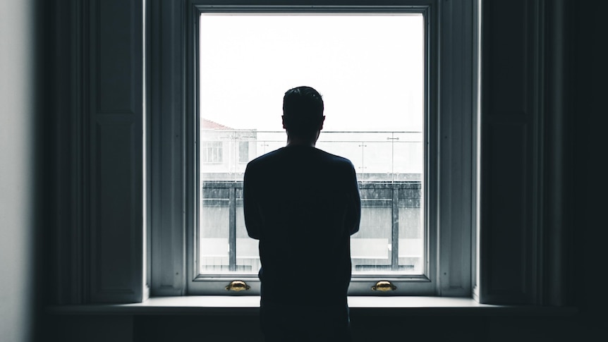 A man is silhouetted against a window. He's looking out it.