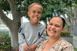 A young boy with dwarfism laughs with his mother in an intimate photograph in the park