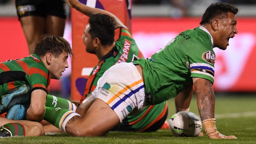 A male NRL player on his hands and knees screams out as he celebrates a try.