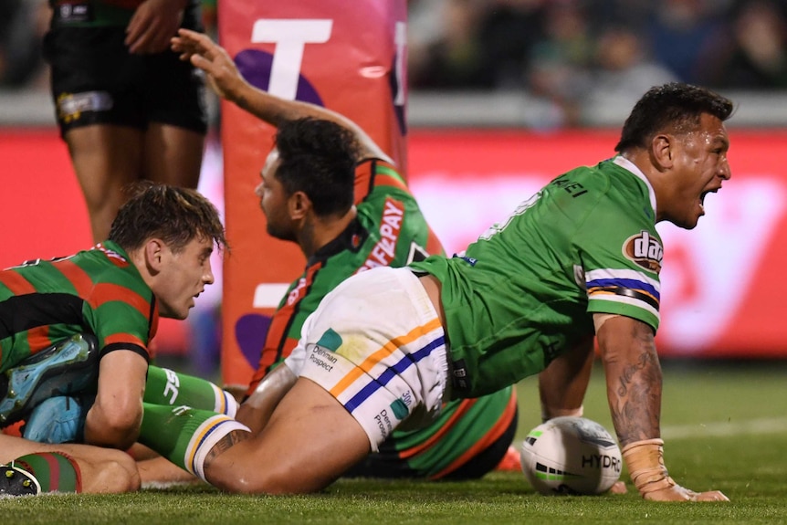 A male NRL player on his hands and knees screams out as he celebrates a try.