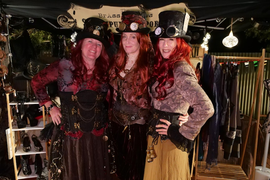 three women with red hair dressed in 19th century dressed pose against their costume stall. 