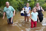 Family wading through floodwaters with cat