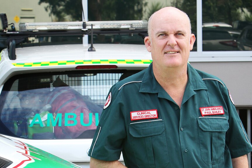 A balding man standing near an ambulance