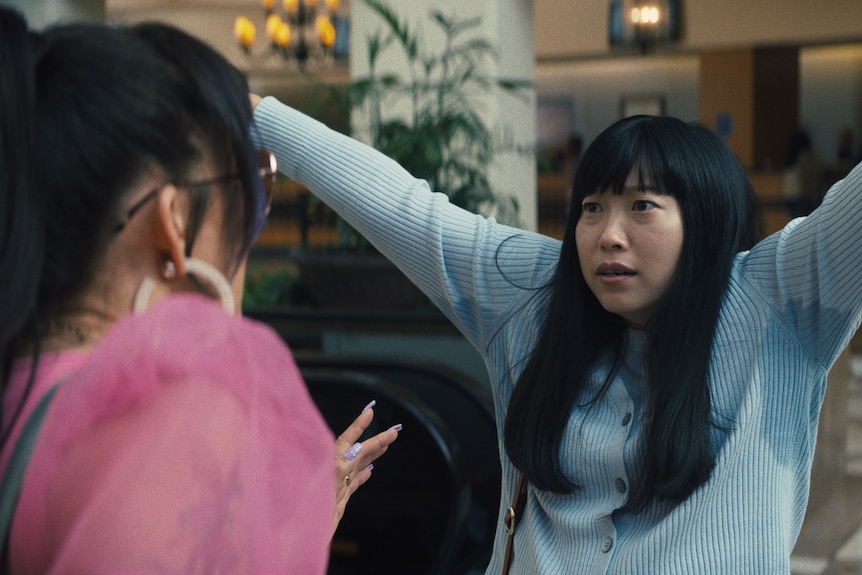 Awkwafina holds up her arms to Sandra Oh to show big sweat patches on her blue top