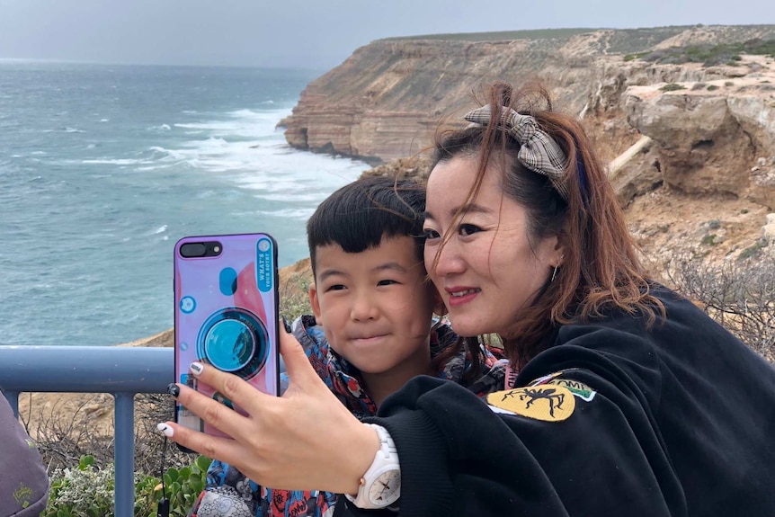 A woman and young boy take a selfie in front of a jagged stretch of WA coastline.