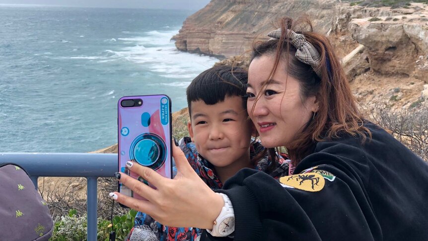 A woman and young boy take a selfie in front of a jagged stretch of WA coastline.