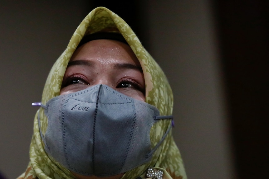 A woman in a hijab and mask sits in an Indonesian court.