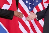 Close up shot of Kim Jong-un and Donald Trump about to shake hands against the background of their country's flags.