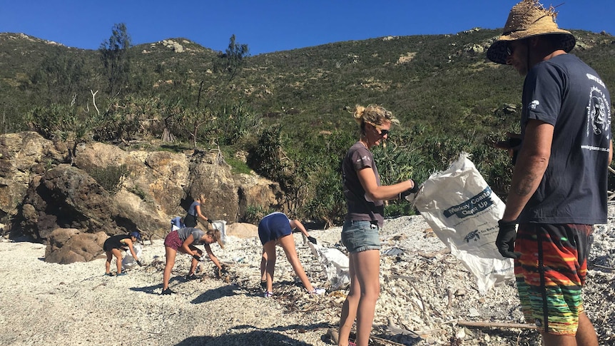 A group of six people clean up rubbish on a beach