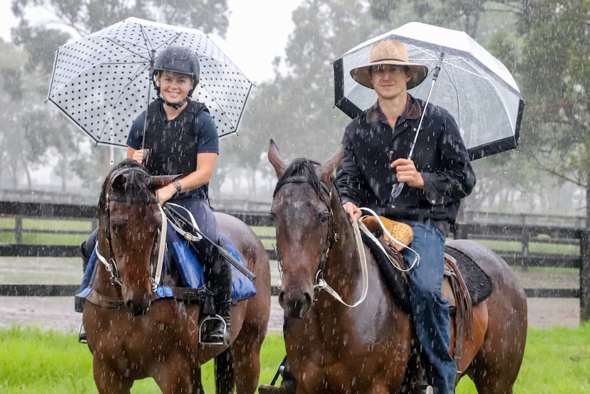 Two horses with riders and umbrellas in the rain.