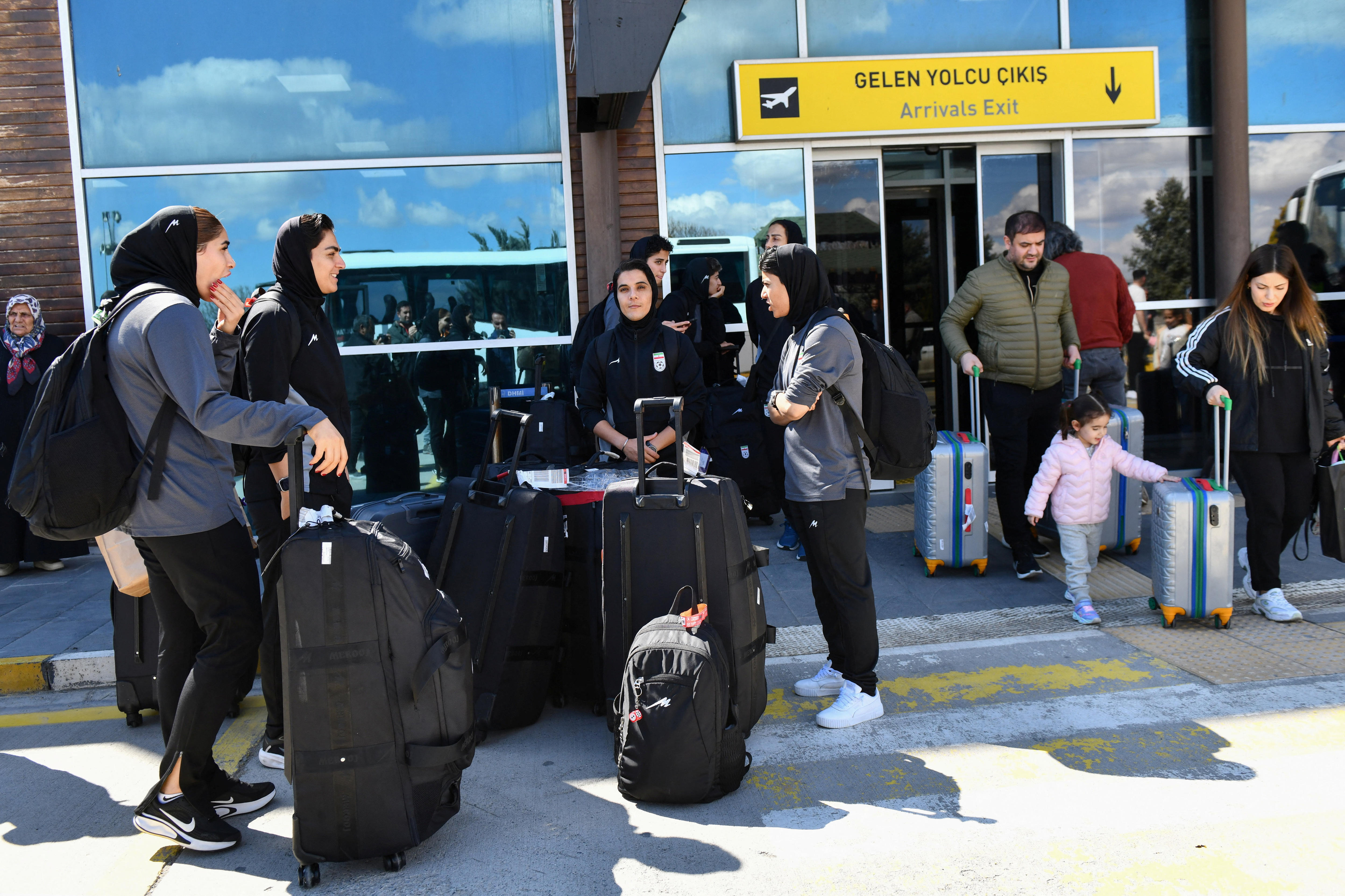 A group of women's football players standing out the front of an airport terminal.
