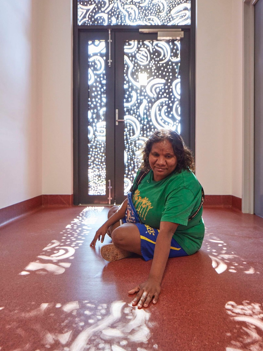 a woman sitting on a floor with sunlight showing through screens