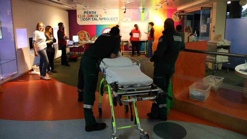 Staff members stand inside a foyer of Princess Margaret Hospital with two paramedics alongside a stretcher.