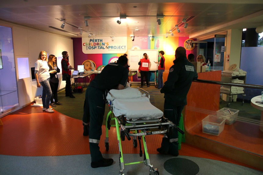 Staff members stand inside a foyer of Princess Margaret Hospital with two paramedics alongside a stretcher.