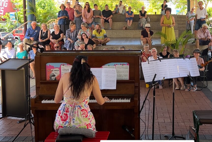 A woman plays a piano and one plays the violin in front of an audience 