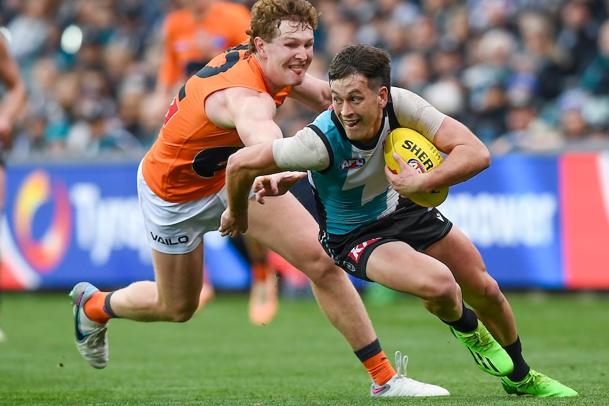 Zak Butters carries the ball as he runs away from Tom Green, who is trying to tackle him