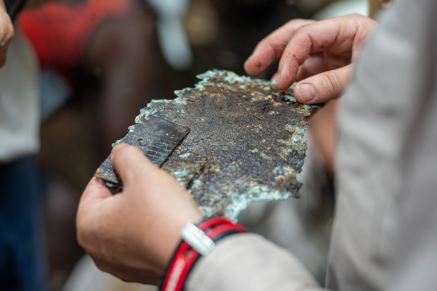A man holds an old piece of metal that has rusted.