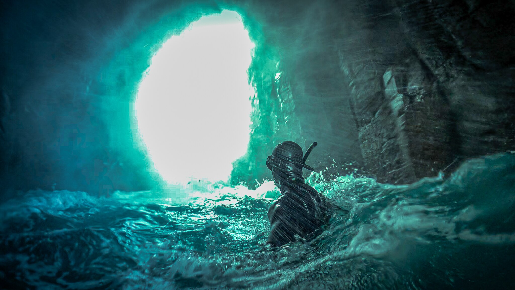 A swimmer in the ocean looks out at a large opening in a rock wall.