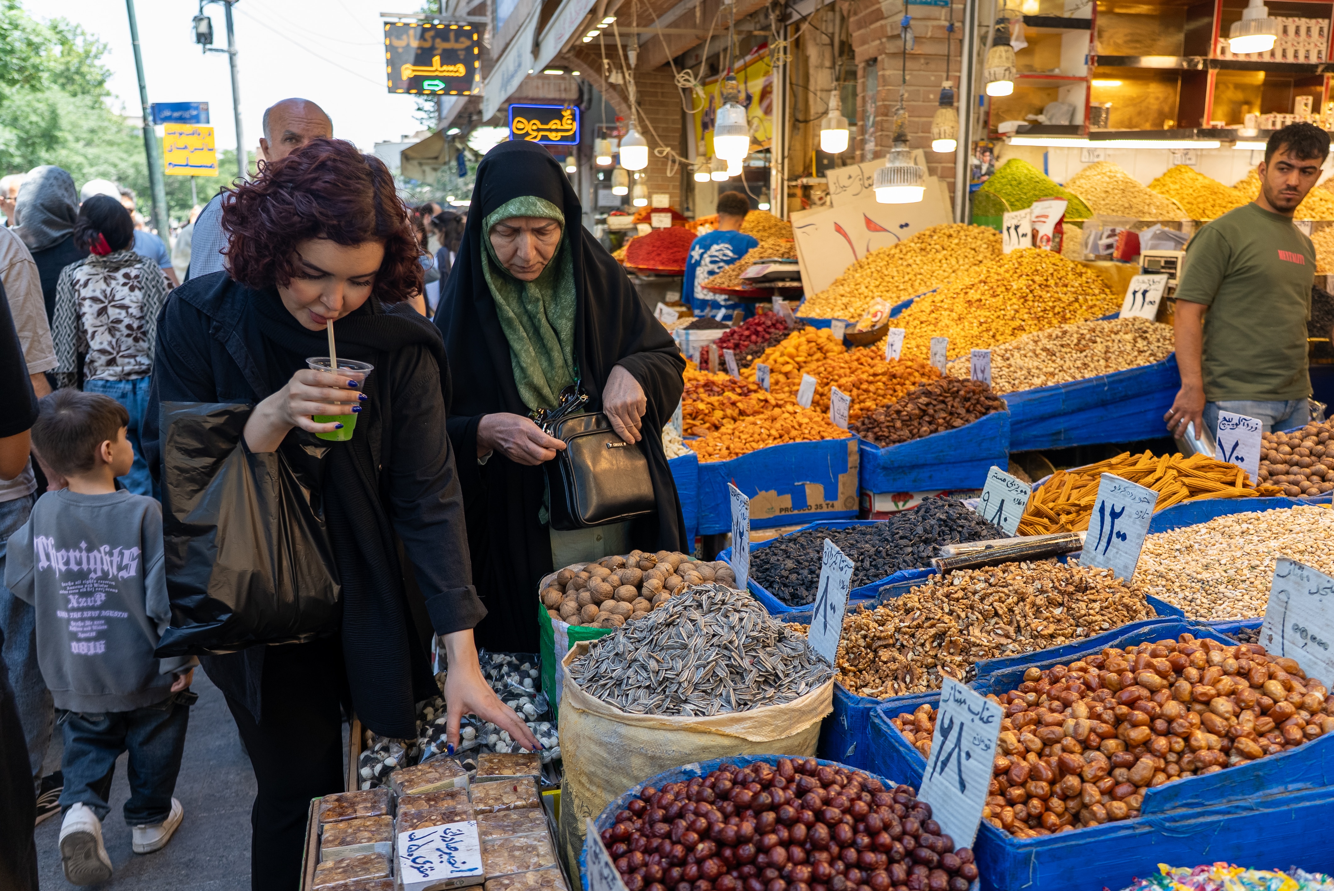 Two women walking past a market stall and inspecting produce.