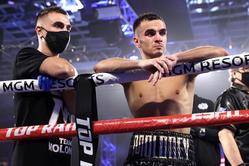 Andrew Moloney stands leaning on the ropes of a boxing ring next to Jason Moloney