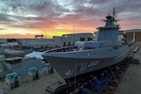 A large naval ship sits on a dock at sunset. 