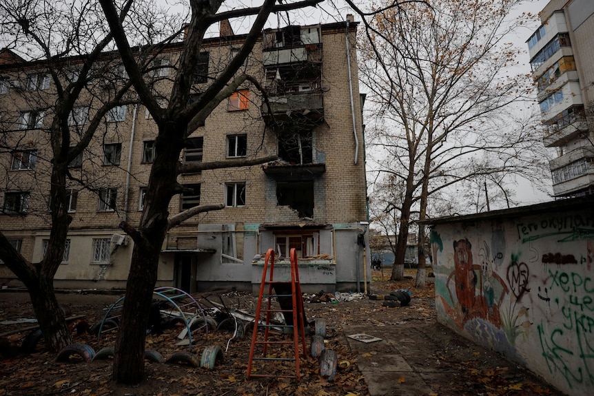 An apartment building damaged by a military strike, with a shabby playground in front.