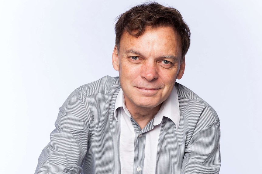 Portrait of a man wearing a striped shirt while sitting in front of a white background.