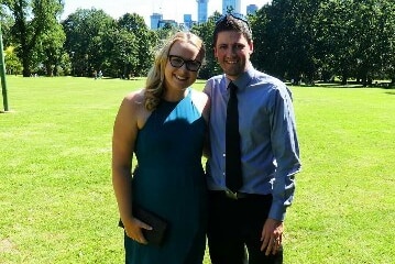 Teagan Sloman smiles as she stands next to her husband Jay in a park, with the city of Melbourne the backdrop.