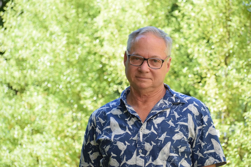 Dr Ross Kirkman in whale-motif shirt with glasses looks at camera. There are green trees in the background.