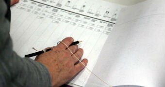 A voter holds a tethered pencil in their right had as they fill out a Senate ballot paper