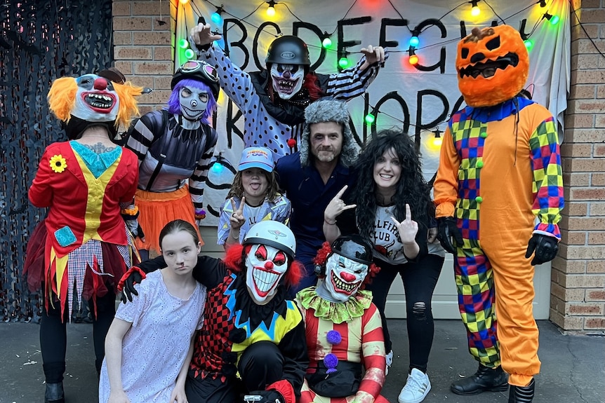 A group of costumed clowns pose in front of a decorated house garage