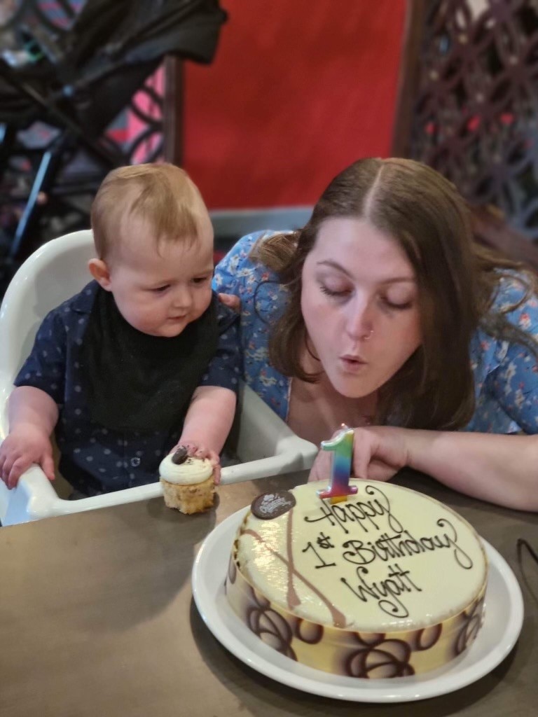 A mother and child blow out candle on a first birthday cake.