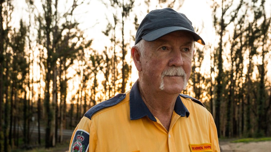 Man in RFS uniform standing at his cleared property with sun going down in the forest behind him.
