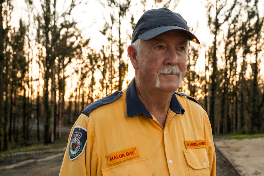 Man in RFS uniform standing at his cleared property with sun going down in the forest behind him.