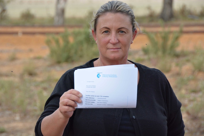 A woman stands outdoors holding up a ouece of paper relating to an internet complaint.