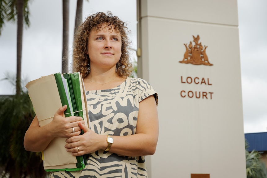 A woman with curly hair and a printed top holds a stack of paperwork outside Darwin local court.