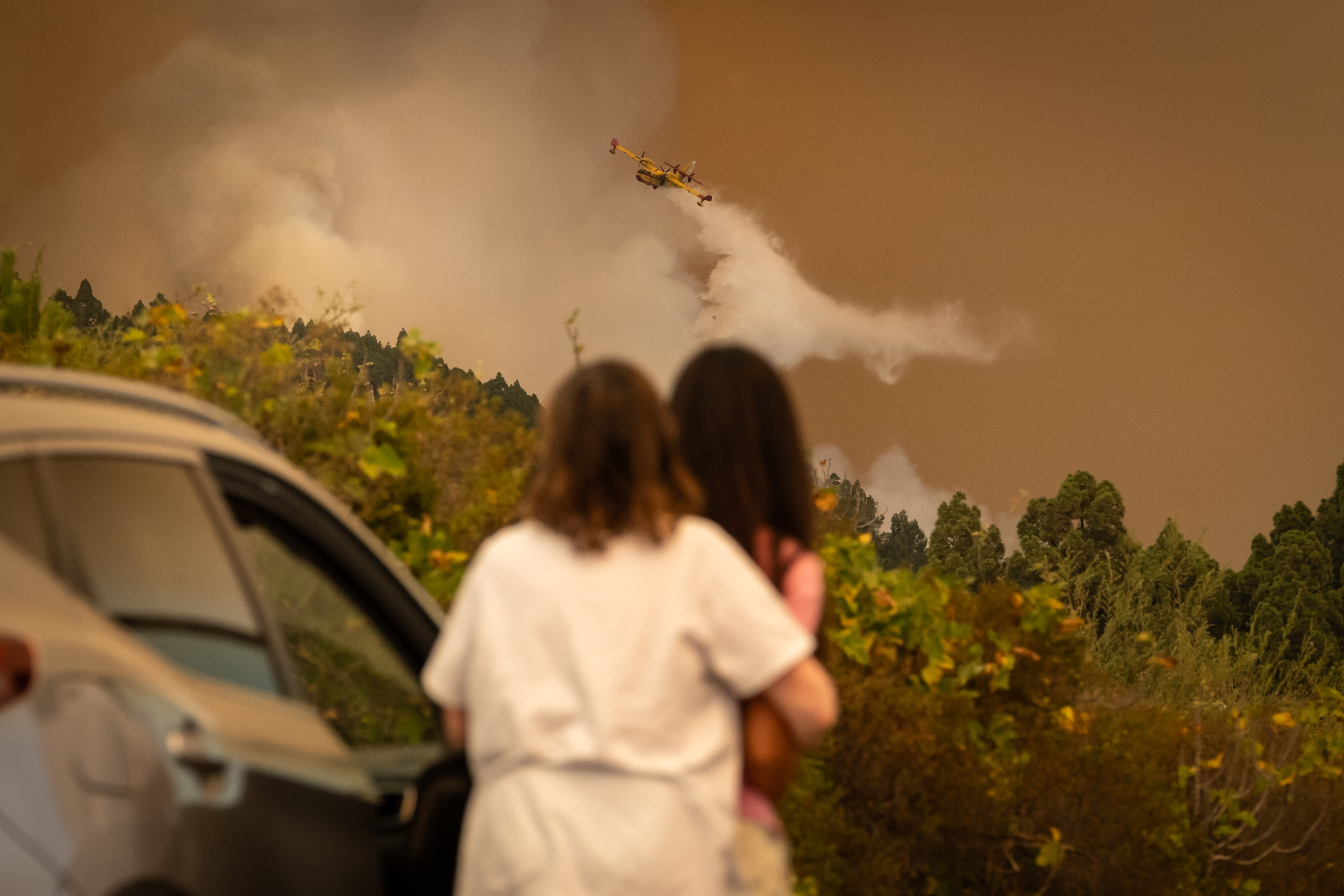 People watch as a helicopter dumps water on a fire.