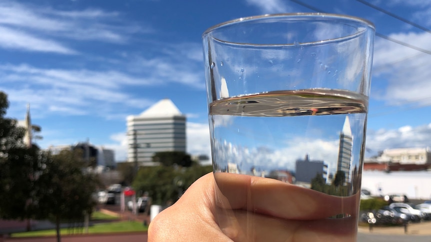 A hand holding a glass of water with a building visible through the water in glass.